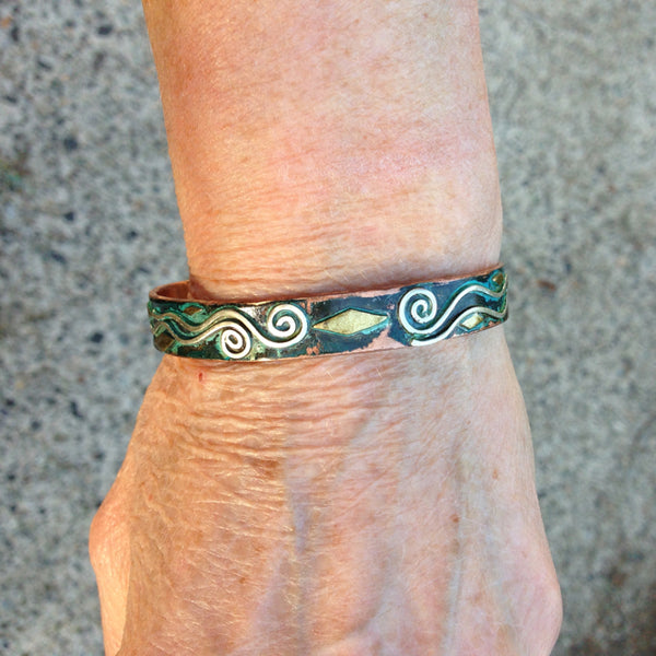 silver spirals on top of a wide copper bracelet with little brass accents and green patina