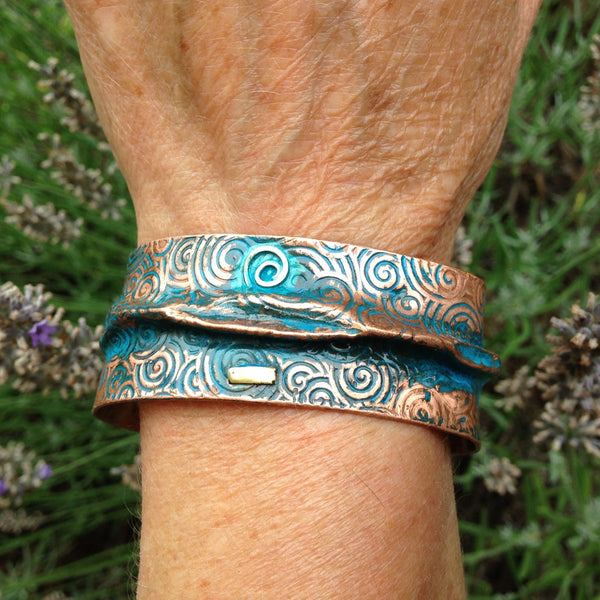 wide folded copper bracelet with embossed spiral pattern, blue-green patina, silver spiraland brass accent.