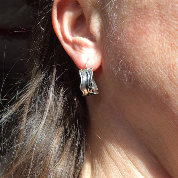 Sterling silver hoops with 3 spirals and waves, black patina in recessed parts and clasps that close behind the ear worn by a person.