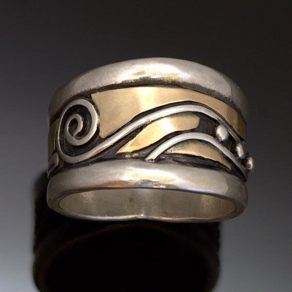 Wide large silver band for men with raised rounded edges, gold, spirals and wave pattern in the centre with recessed parts oxidized.