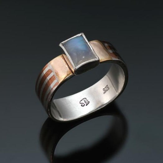 Narrow Silver band with long stripes of silver and copper with a rectangular blue rainbow moonstone and gold beside the stone.