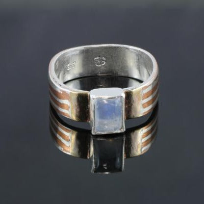Narrow silver band with silver and copper stripes with a rectangular rainbow moonstone and gold on either side of the stone.