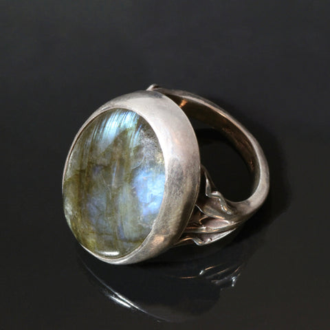 silver ring with oval 18x25mm blue and green labradorite set into a bezel setting. The ring is narrow on the inside, widening towards the stone with lines of silver waves and a star on either side of the labradorite