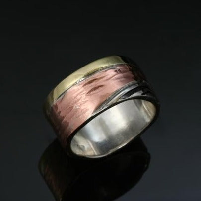 11mm Sterling silver band made with a narrow brass band beside a slightly hammered copper band beside a silver wave with recessed parts oxidized black. 