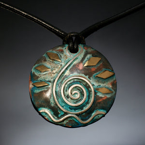 round copper pendant with silver spiral design treble clef, waves and brass accents aged green patina