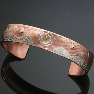 copper bracelet with textured silver shaped like mountains with a silver gold sun and 6 gold circles above the mountains