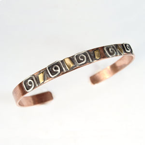 narrow copper bracelet with 5 square silver spirals and 4 brass accents in-between with black patina