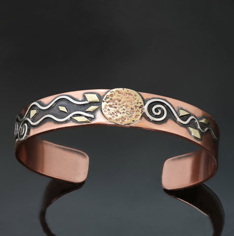 wide copper coloured bracelet with silver spirals and hammered brass disc in the middle with black patina