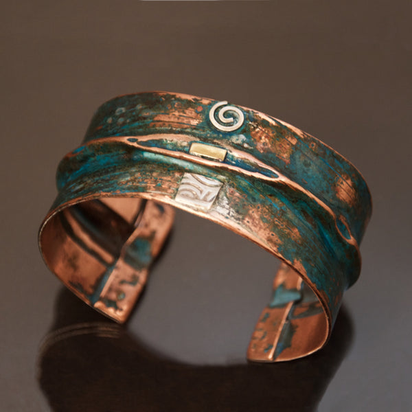 wide folded copper bracelet with blue-green patina and embossed denim pattern. Sterling silver spirals and brass accents.