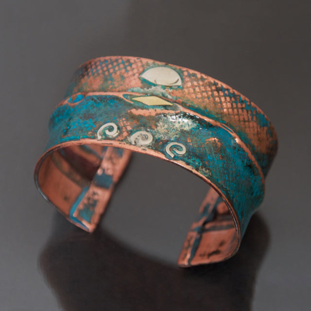 wide folded copper bracelet with blue-green patina and embossed denim pattern. Sterling silver spirals and brass accents.