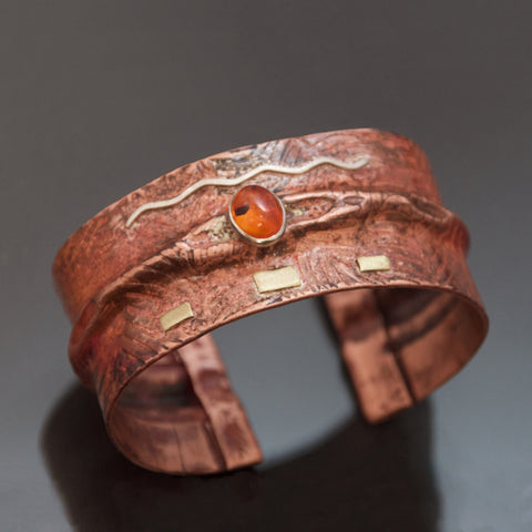folded copper bracelet with a fern pattern embossed, silver and brass with brown copper patina and oval amber
