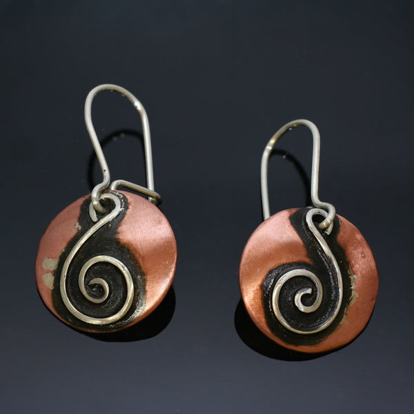 round copper earrings with silver spiral shaped like a treble clef and black patina