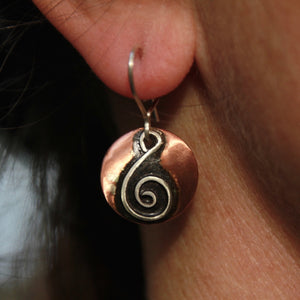 round copper earrings with silver spiral shaped like a treble clef and black patina hanging from an earlobe