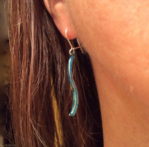 long skinny copper earrings with blue patina, a silver wire down the centre the earring is s-shaped hanging from an earlobe