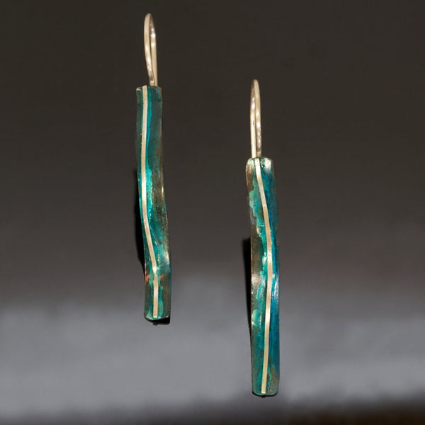 long skinny copper earrings with blue patina, a silver wire down the centre, the earring is s-shaped.