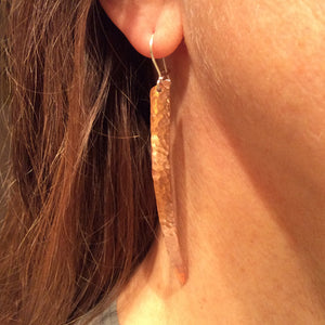 long and narrow hammered copper Earrings hanging from an earlobe