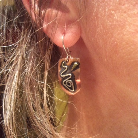 Larger copper earrings with a silver fish design, brass and black patina on an ear lobe