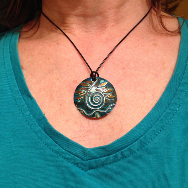 round large copper necklace with blue/green patina, silver wave and spiral shaped like a clavicle, brass accents on a leather band
