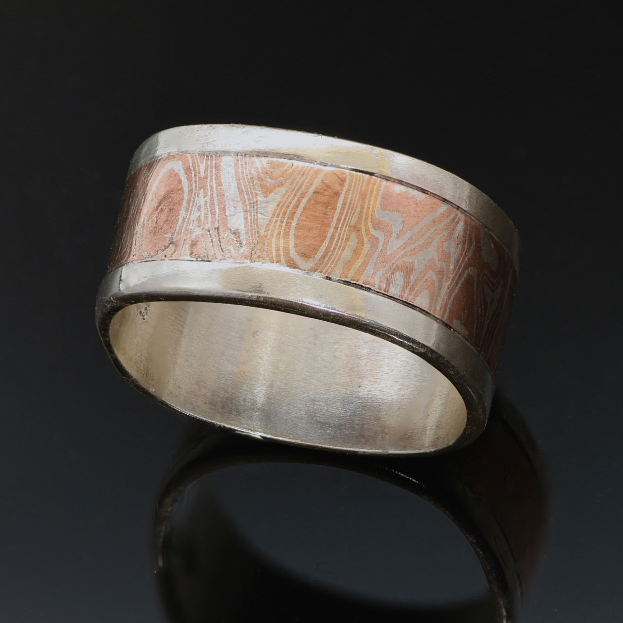 11mm wide Silver band with a centre band of mokume gane. The mokume has a wavy wood grain pattern and is made with copper and silver.  