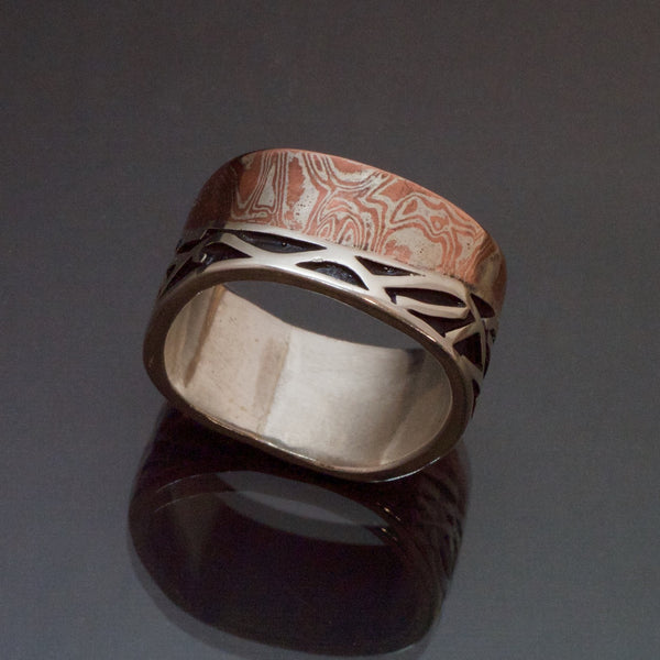 Sterling silver band made with an band of mokume gane contouring waves of sterling silver with recessed parts oxidized black. The mokume is made with copper and silver. 