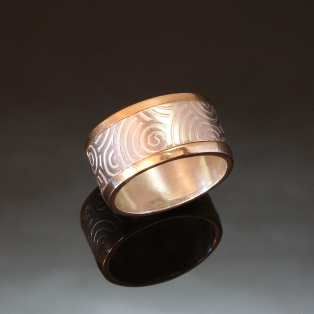 wide silver ring with spirals embossed and gold rails on the outside edges of the band