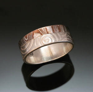 Silver band made with embossed spirals beside a band of mokume gane. The mokume is made with copper and silver. 