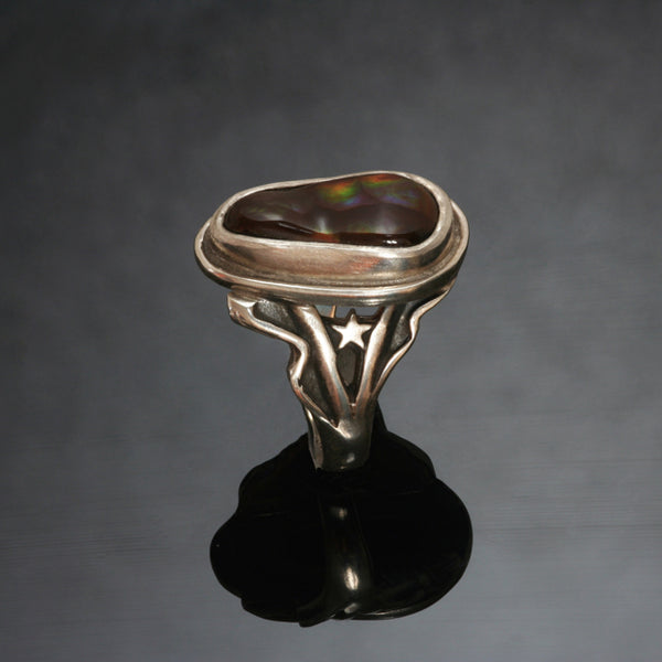 silver ring with irregular shaped fire agate set into a bezel setting. The ring widens towards the stone with lines of silver waves and a star on either side of the fire agate. 