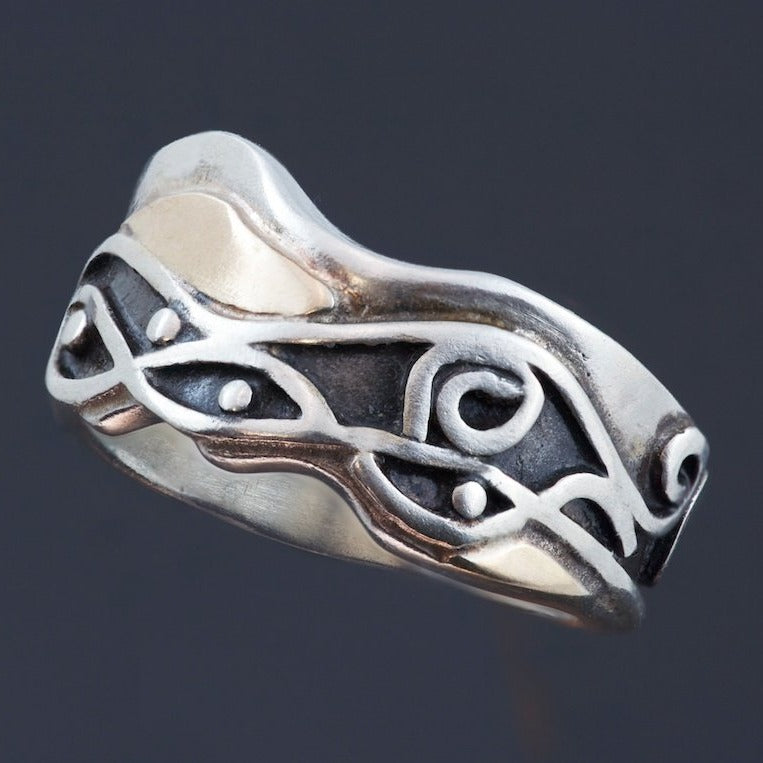 Silver ring with uneven edges, waves, spirals and recessed parts oxidized. There are wavy gold accents around the pattern.