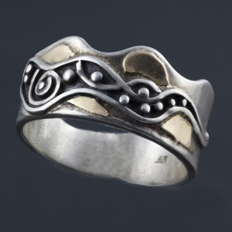 Silver ring in a crown shape with flowing waves and spiral and gold accents around the pattern.