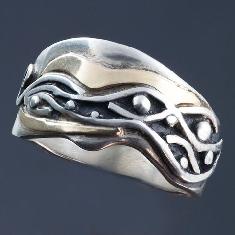 Silver band with wavy edges, raised wave pattern with silver dots, a spiral on one end and gold accents around the pattern. The pattern is oxidized black.