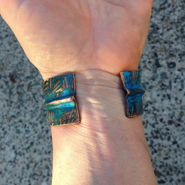 Inside of a wide folded copper bracelet on an arm with the ends folded to have smooth edges.